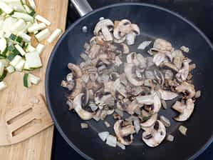 cebolla y champiñones en un sartén con trozos de calabacín al lado