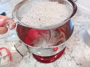 tamizando los ingredientes secos sobre el tazón con la masa de tarta red velvet