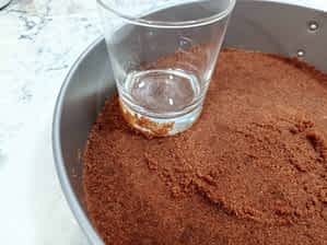 aplastando con un vaso la masa de base de galletas en el molde