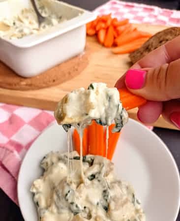 dip de espinacas y alcachofas en un palito de zanahoria