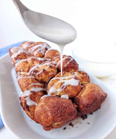 una cuchara rociando el glaseado sobre el pan de canela