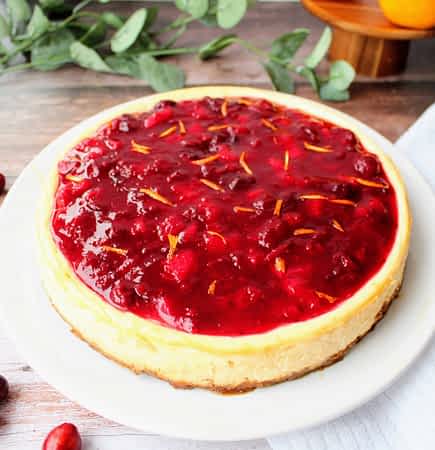 cheesecake entero en un plato con salsa de arándanos rojos