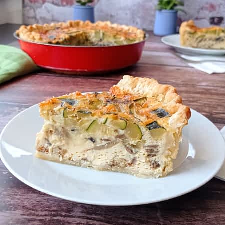 un trozo de quiche de calabacín y champiñones en un plato en frente del quiche enero