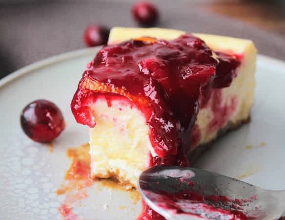 un trozo de tarta de queso con arándanos rojos y naranja