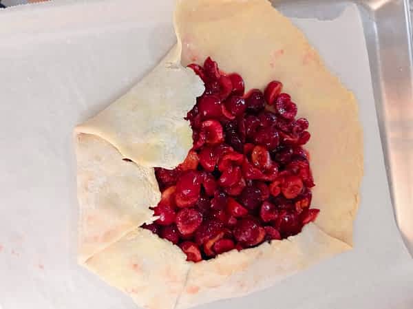 Dobla la masa hacía adentro, dejando un espacio descubierto en el centro. el galette en una bandeja con la mitad de sus bordes doblado hacía adentro