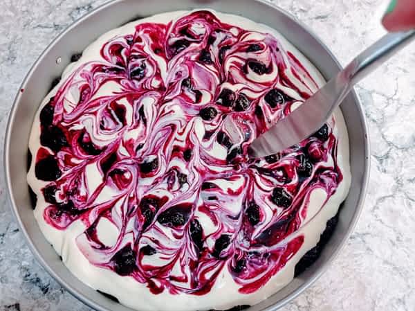 Esparcir el resto de la salsa de fruta; pasar el punto de un cuchillo en círculos por la parte superior. haciendo decoración en la superfície del cheesecake con un cuchillo