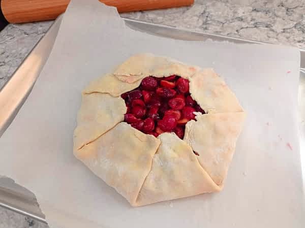 Continúa doblando todos los bordes. el galette con forma redonda en la bandeja