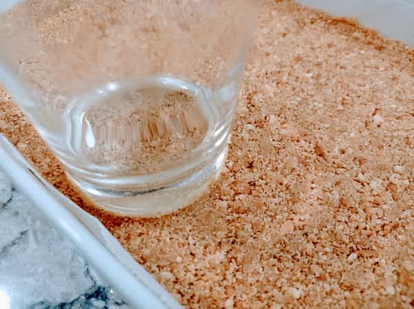 un vaso de cristal encima de la base de galleta utilizado para aplanarla