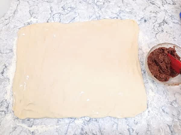 la masa en forma rectangular en la encimera al lado de un tazoncito con el relleno