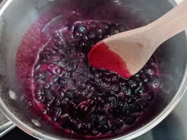 Hervir lentamente la fruta hasta que se blande. Opcionalmente triturar la salsa o dejarla con trozos de fruta. la salsa de arándanos herviendo en la olla