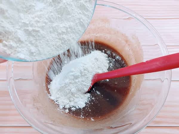 echando harina en el tazón con los ingredientes húmedos