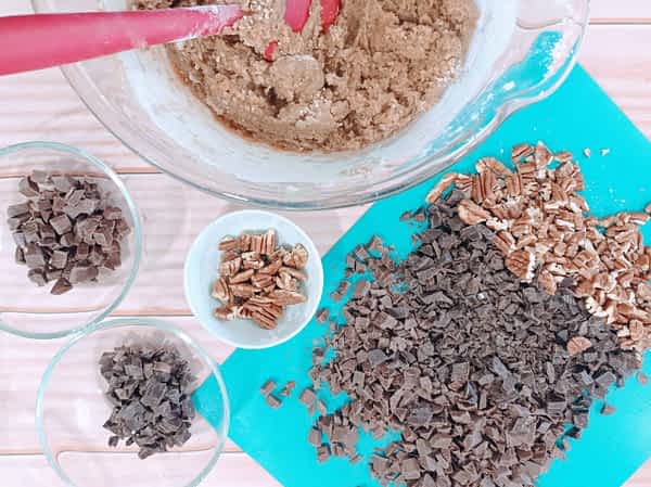 un tazón grande de masa de galletas con bols de chocolate y nueces troceados alrededor