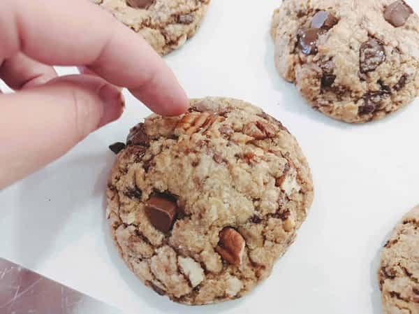 una mano presionando una pecana en la parte superior de una galleta de chocolate