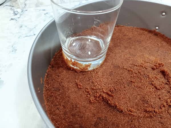 Aplastar la mezcla de galletas en el fondo del molde forrado. Ponerlo en la nevera. aplastando con un vaso la masa de base de galletas en el molde