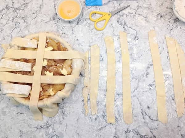 Doblar cada otra tira hacia un lado. Coger la tira más larga de la mesa y ponerla perpendicular en el medio del pay. empezar con el centro