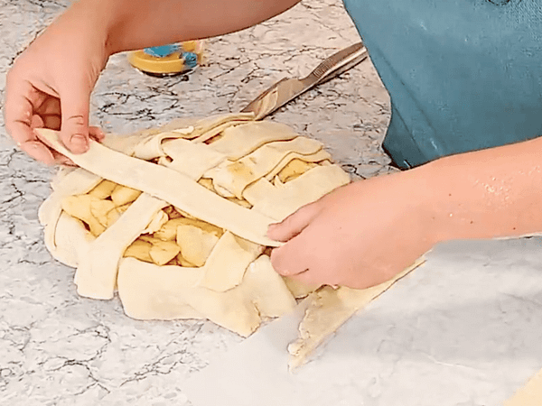 Desdoblar las tiras y doblar hacia atrás las tiras alternas. Poner otra tira de masa encima del pay. poner tiras de masa encima del relleno