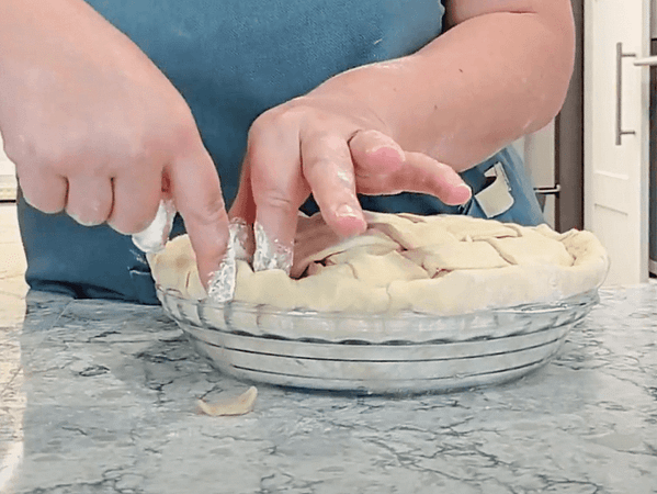 Rizar el borde usando una pinza con el dedo índice de una mano y el dedo índice más el pulgar de la otra mano (todos bien enharinados). rizar los bordes de la masa con los dedos
