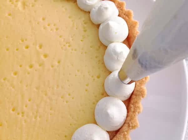 usando una manga pastelera para poner la nata montada encima de la tartaleta de limón