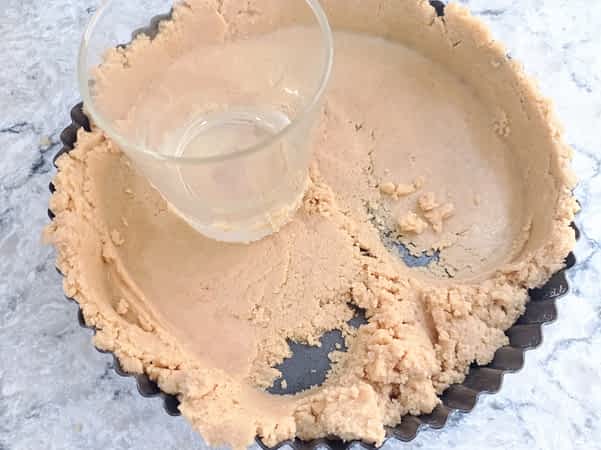 usando un vaso de cristal para presionar la base de galletas a los lados del molde