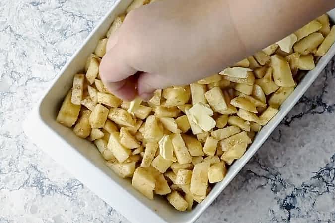 colocando trozos de mantequilla encima de las manzanas en el molde